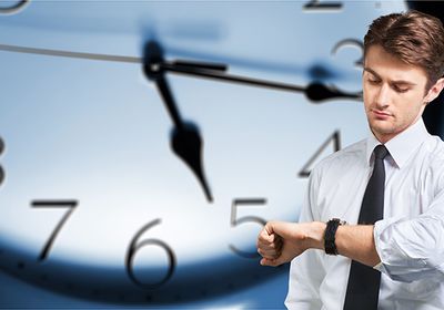 Mann schaut auf Armbanduhr, Große Wanduhr im Hintergrund