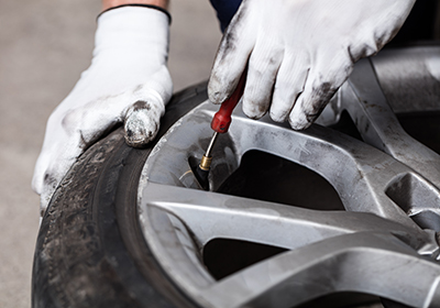 Hände in Handschuh lassen Luft aus liegendem Reifen entweichen